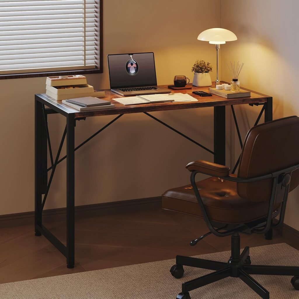 Escritorio plegable de estilo industrial con tablero de madera y estructura metálica negra, decorado con una lámpara moderna, laptop y accesorios de oficina, acompañado de una silla giratoria de cuero marrón.