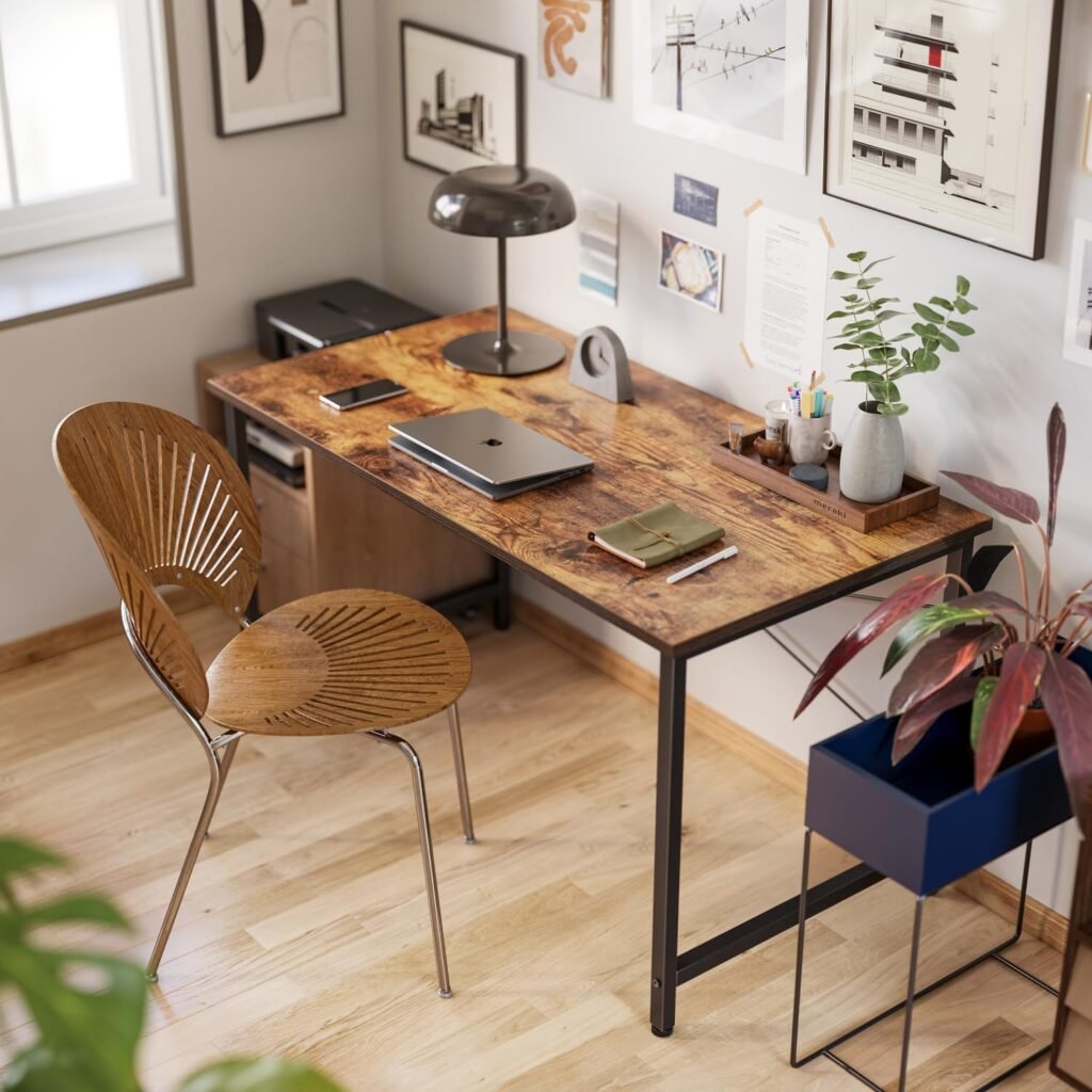 Escritorio de estilo industrial con tablero de madera y estructura metálica negra en una oficina en casa decorada con arte en las paredes, plantas y accesorios de escritorio.