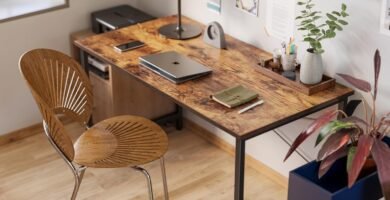 Escritorio de estilo industrial con tablero de madera y estructura metálica negra en una oficina en casa decorada con arte en las paredes, plantas y accesorios de escritorio.