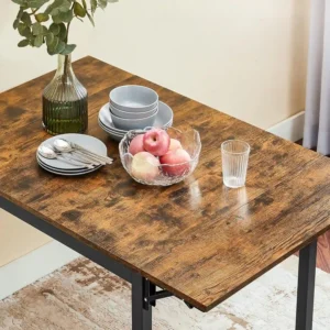 Comedor plegable de madera rústica con estructura metálica negra decorada con vajilla gris, un cuenco de vidrio con manzanas, un vaso y un jarrón de cristal con eucalipto.