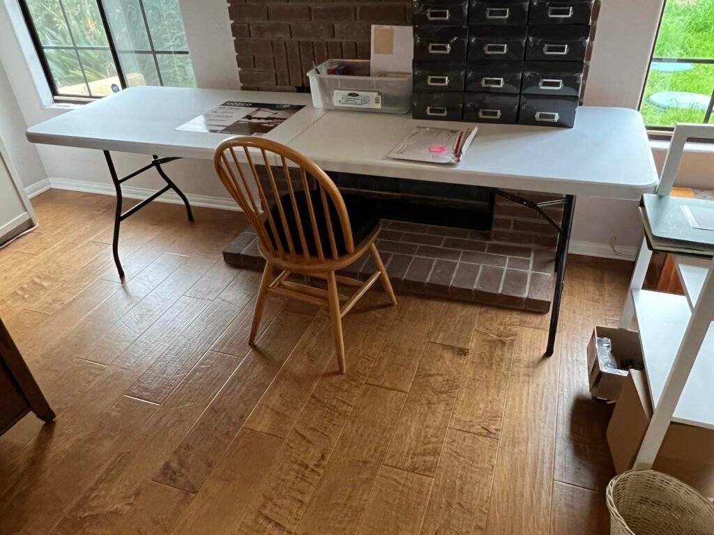 Mesa plegable blanca de seis pies usada como escritorio, con silla de madera y cajas organizadoras.