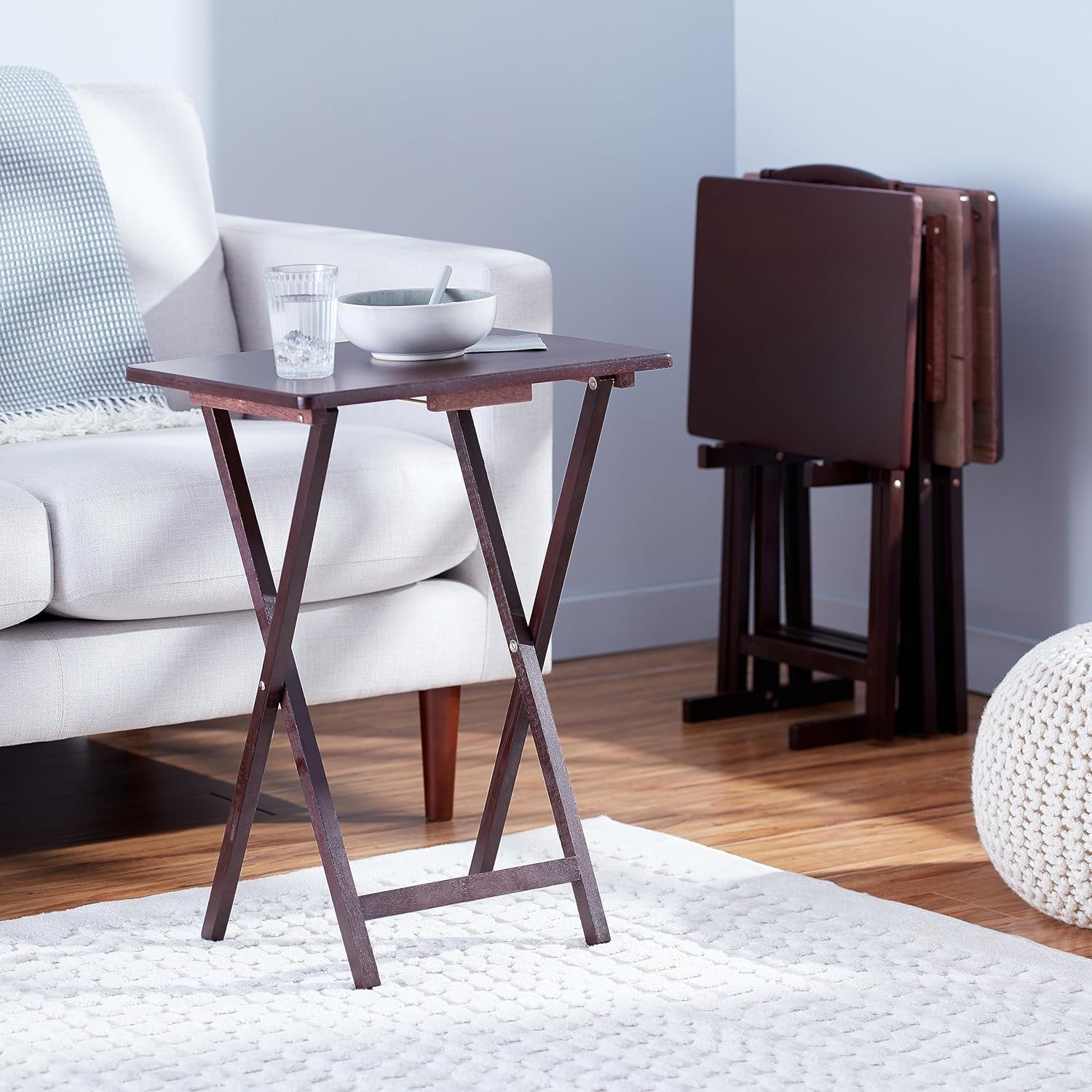 Mesa plegable pequeña de madera junto a un sofá blanco, con un vaso y un tazón encima.