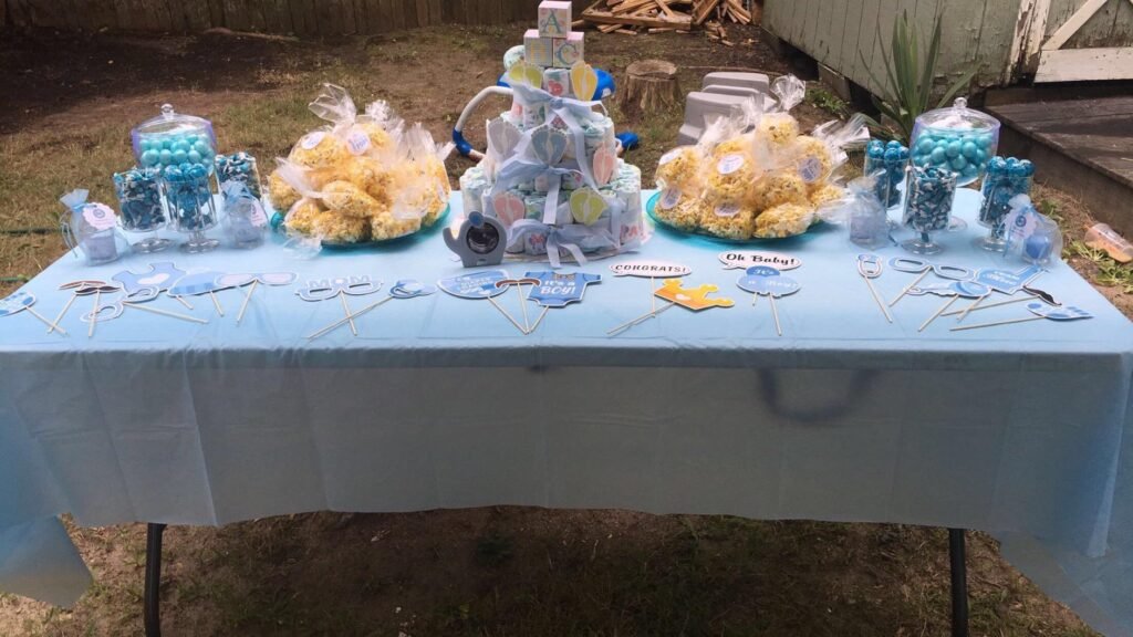Mesa decorada con tema de baby shower en tonos azules, con dulces y adornos en un jardín al aire libre.