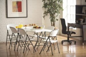 Conjunto de mesa plegable blanca de 6 pies con sillas plegables en un comedor moderno con paredes de ladrillo blanco y piso de madera.