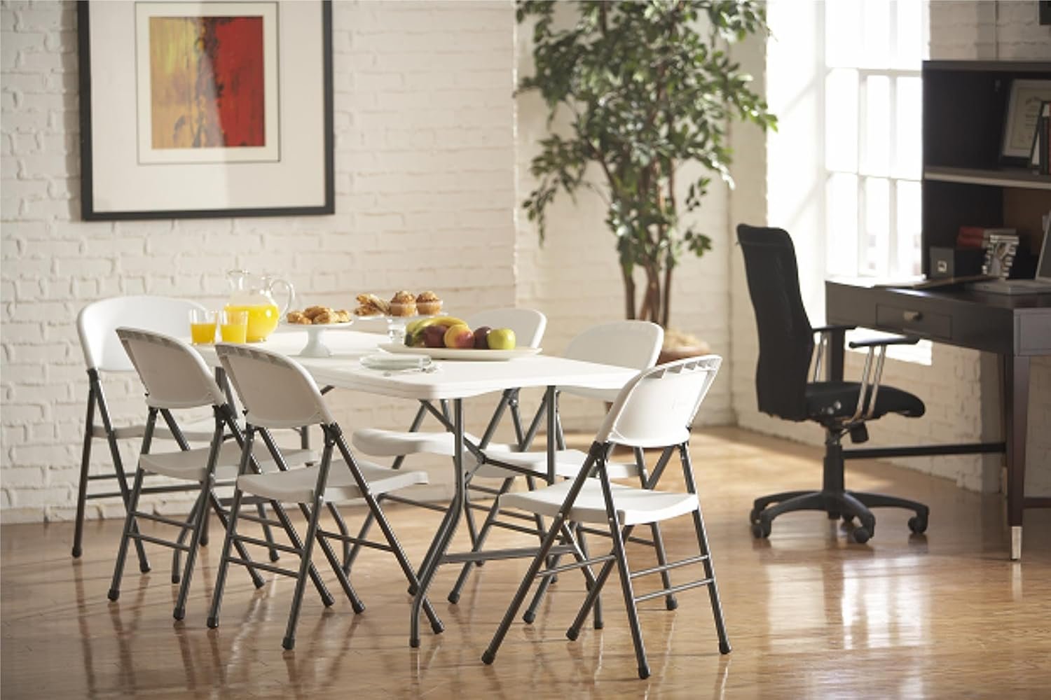 Conjunto de mesa plegable blanca de 6 pies con sillas plegables en un comedor moderno con paredes de ladrillo blanco y piso de madera.
