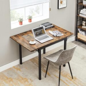 Escritorio plegable de estilo industrial con tablero de madera rústica y estructura metálica negra, decorado con una laptop, una taza de café y revistas, acompañado de una silla gris en una oficina en casa iluminada.