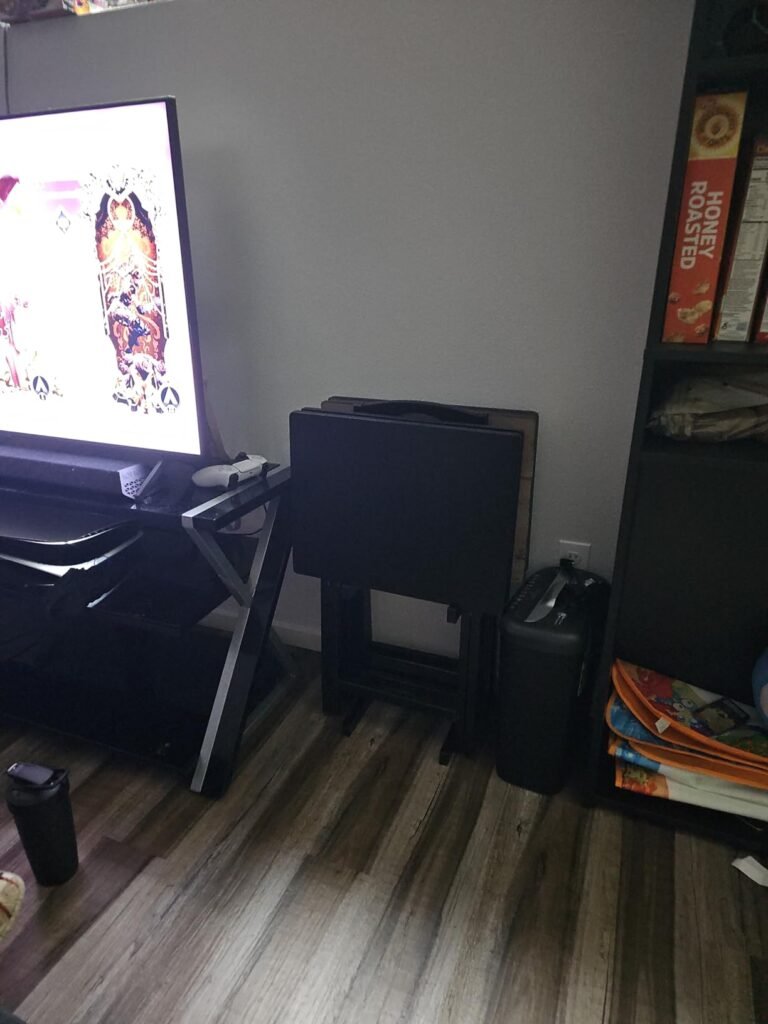 Conjunto de mesas plegables de madera oscura almacenadas junto a un televisor y una estantería en una sala de estar.