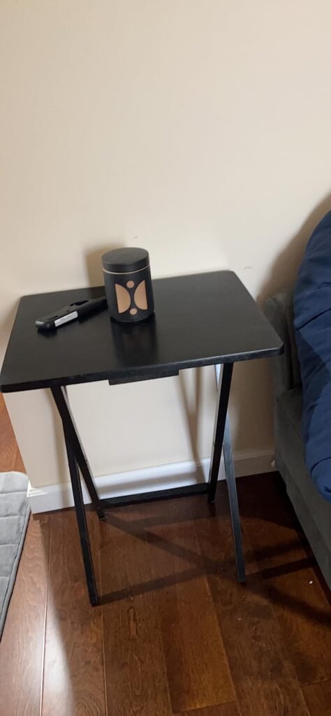 Mesa plegable de madera oscura con un recipiente y un encendedor, colocada junto a un sofá en una habitación.
