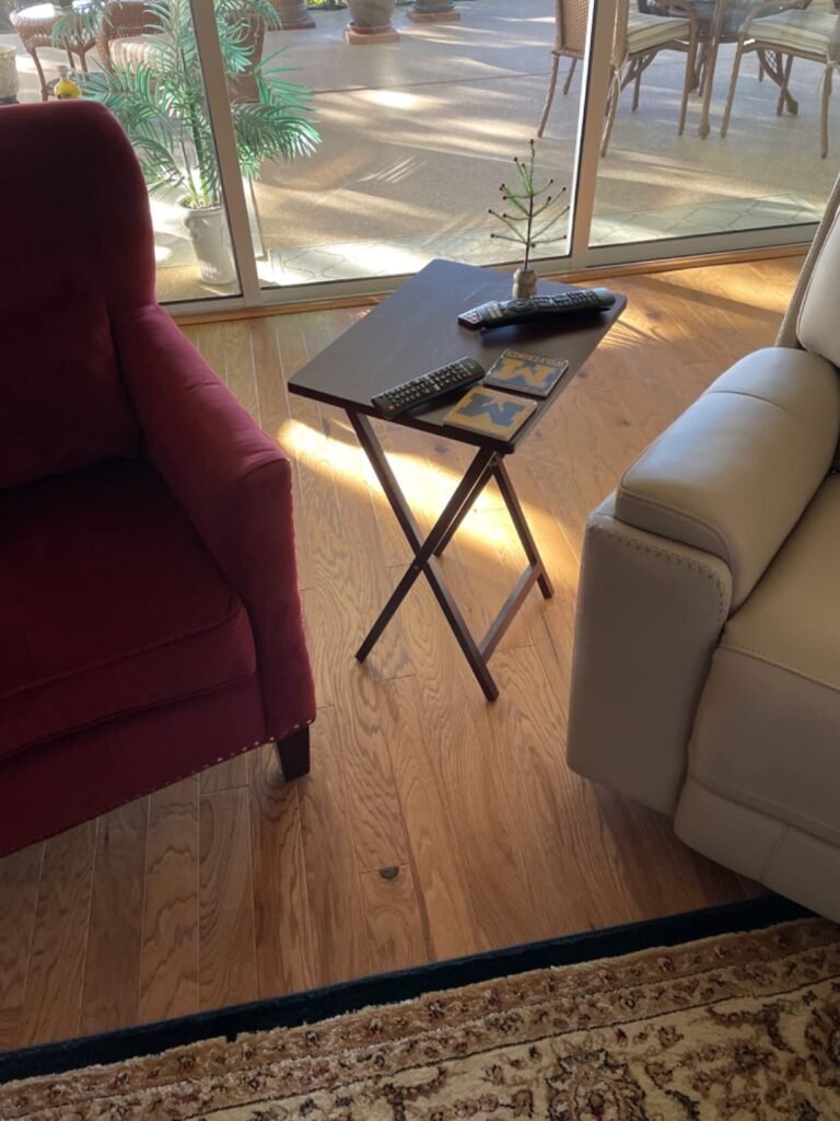 Mesa plegable de madera oscura en una sala de estar entre un sofá rojo y otro beige, con controles remotos y una decoración pequeña encima.