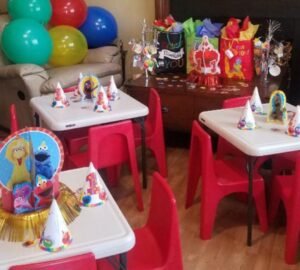 Decoración de fiesta infantil con mesas plegables Lifetime blancas, sillas rojas de plástico y temática de personajes animados, rodeadas de globos y regalos coloridos.
