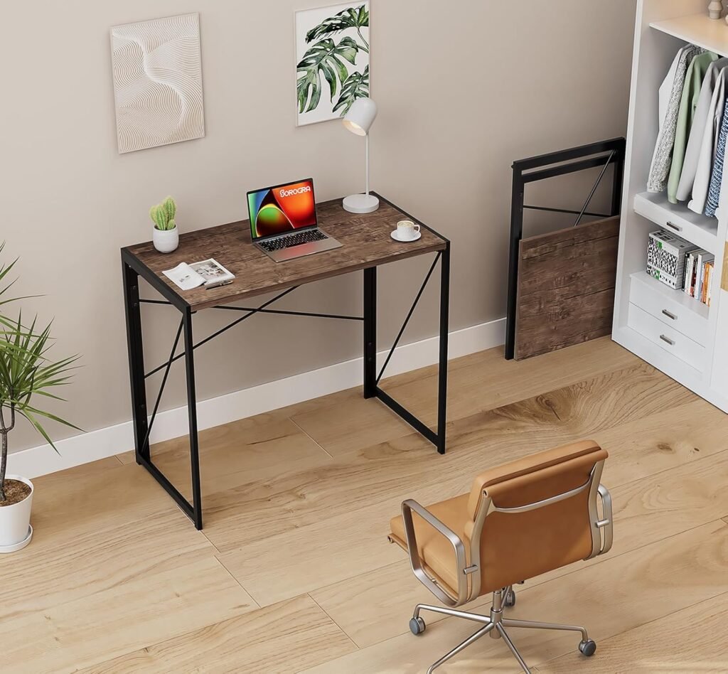 Oficina en casa con escritorio plegable de madera oscura y estructura metálica negra, acompañado de una silla ejecutiva de cuero marrón, una lámpara de escritorio blanca y decoración minimalista.