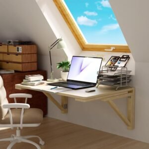 Escritorio flotante de madera clara montado en la pared bajo una ventana inclinada, con laptop, libros, lámpara de escritorio, organizador de documentos y silla giratoria blanca.