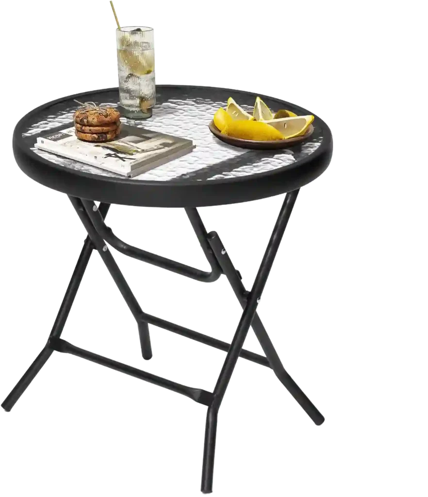 Mesa redonda plegable con estructura metálica negra y superficie de vidrio texturizado, decorada con una bebida, galletas, libros y un plato con rodajas de limón.