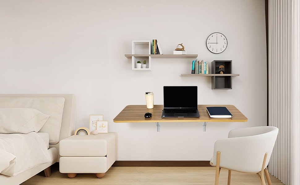 Dormitorio moderno con escritorio flotante de madera clara resistente montado en la pared, equipado con laptop, taza, mouse y libreta, junto a una cama, silla blanca y repisas decorativas.