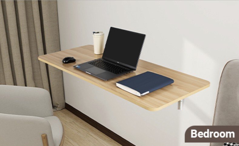 Escritorio flotante de madera clara montado en la pared de un dormitorio, con laptop, cuaderno azul, mouse y taza, acompañado de sillas modernas y cortinas beige.